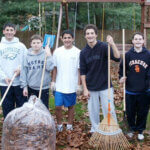 Students raking leaves and smiling for photo