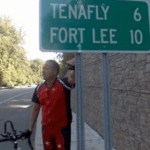 Man standing near mile marker sign that says "Tenafly 6" and "Fort Lee 10"