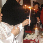 church official holding lit candle. Other church members are in the background